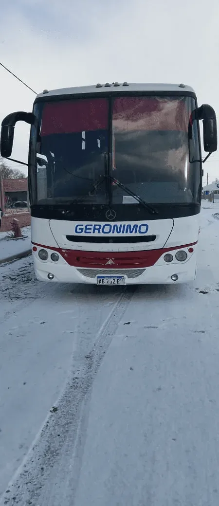 A white and red bus named "GERONIMO" is parked on a snowy street, with a clear windshield and visible headlights.