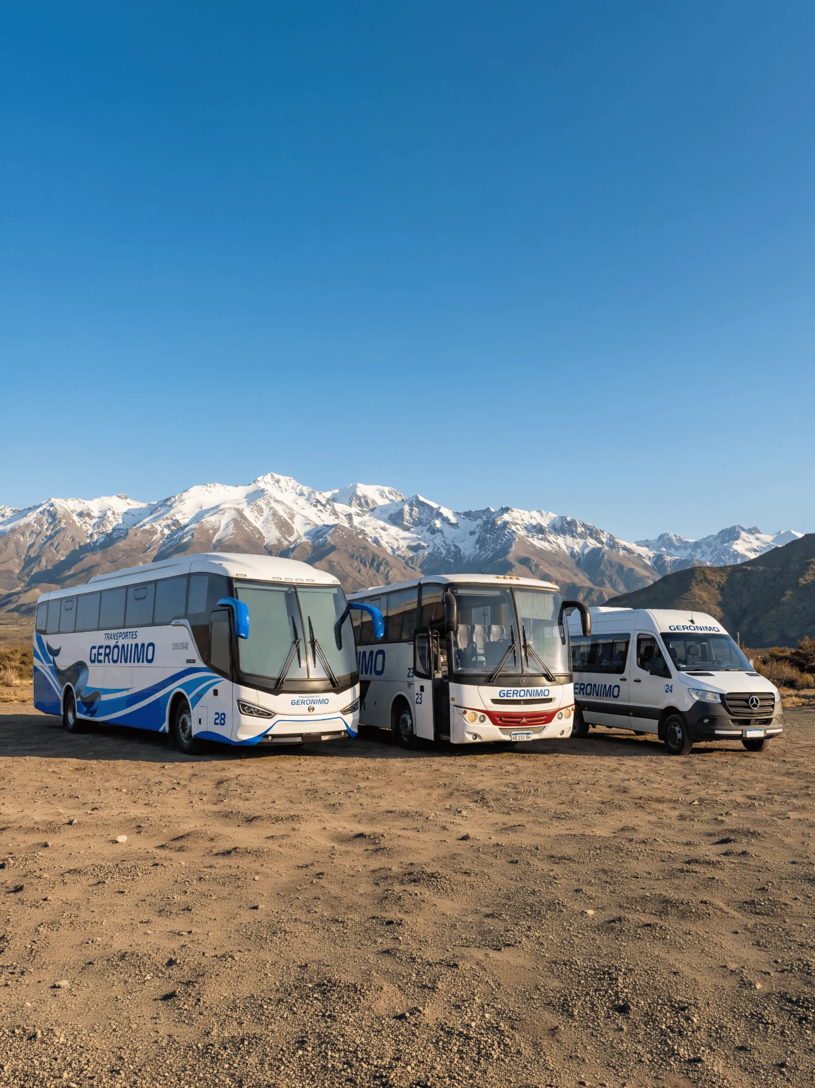 A white tour bus with the name "GERONIMO" travels along a scenic mountain road under a clear blue sky.